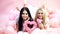 Girls lay near balloons, holds heart toys, pink background. Valentines day concept. Blonde and brunette on smiling faces