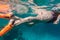 Girls legs in orange flippers dive underwater in sea near coral