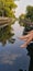 Girls point feet into clear and quiet canal that full of sky and tree reflection