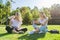 Girls students sitting on green lawn with digital tablet, drink bottle of water