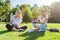 Girls students sitting on green lawn with digital tablet, drink bottle of water