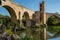 Girona, Spain - Sept 24 2018: View from under the romanesque bridge across Fluvia river with arches and defence towers in Besalu,