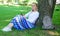 Give yourself break and enjoy leisure. Girl sit on grass lean on tree trunk relaxing in shadow green nature background