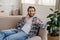 Glad attractive millennial caucasian guy with stubble speaks on phone in living room interior