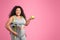 Glad black body positive woman in sportswear holding apple and scales, enjoying diet result, pink background, copy space