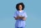 Glad black millennial lady nurse in uniform making notes, isolated on blue studio background