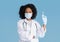 Glad black millennial woman doctor in white coat, protective mask, gloves show syringe