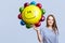 Glad brunette woman wears striped blouse, holds balloon, happy to celebrate daughter`s birthday, meets guests, isolated over blue