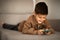 Glad caucasian little child in casual watching video on smartphone, lies on sofa, enjoy spare time in living room