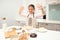 Glad caucasian small girl in apron making cookie dough, has fun, showing hands in flour in kitchen interior