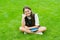 glad child in glasses sitting on green grass with book