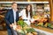 Glad couple is standing with cart with products in supermarket