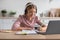 Glad european youngsters girl blonde pupil in headphones makes notes, study at home at table