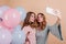 Glad girl with trendy wavy hairstyle using phone for selfie with friend. Lovable young woman with pink balloons