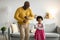 Glad happy african american small girl and old man dancing, have fun in living room interior