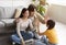 Glad happy asian teen daughter gives high five to young parents sitting on floor in living room interior