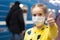 Glad and happy beautiful joy child in the medical helthcare guarding or protecting mask and in yellow t-shirt in subway