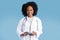 Glad happy black millennial lady doctor in white coat uses phone, chatting, isolated on blue studio background