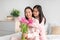 Glad happy japanese teenage girl hugging young woman in pajama, giving bouquet of tulips