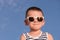 Glad little boy wearing sunglasses on blue sky background