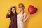 glad mother and daughter hold love heart balloon on yellow background