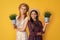 glad mother and daughter with potted plant on yellow background