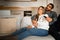 Glad multiethnic millennial couple hug sit on sofa enjoy free time, watch tv together with remote control