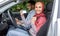 Glad muslim woman in hijab show driving license and fist in open door in car after exam with male teacher