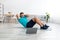 Glad smiling millennial european man doing abs exercises on mat on floor and looking at computer