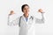 Glad smiling young indian female doctor in coat points fingers at herself, isolated on white background, studio