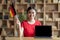 Glad teenage chinese girl hold flag of Germany at table with laptop with blank screen in room interior
