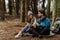 Glad young european guy and woman tourists in jackets with backpack rest in forest camping, enjoy cold season