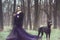 Glam lady in luxurious sequin violet evening gown and fur coat standing in the woods with her Doberman pinscher dog