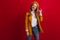 Glamorous blonde woman in beret smiling at camera. Studio shot of charming french female model isolated on red