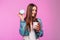 Glamorous funny young woman in stylish denim jacket with cup of tea or coffee posing with donut in mask near the glamorous pink