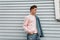 Glamorous pretty young man model in trendy pink sweatshirt in fashion denim blue youth clothes posing near white wall outdoors.