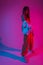 Glamorous young woman dancer in trendy sports youth clothes posing in a room with multi-colored pink-blue color. Attractive girl