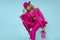 Glamour elegant woman is wearing an elegant fuchsia suit, hat and a pink handbag with spring flowers and is posingob blue