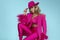 Glamour elegant woman is wearing an elegant fuchsia suit, hat and a pink handbag with spring flowers and is posingob blue