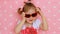 Glamour. Fashion. Beauty. A cute child fashionista plays a real lady. Pink background. Beautiful little girl dresses red