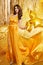 Glamour Woman in Golden Silk Dress Dancing with Party Foil Star Balloons over Sparkling Gold Background. Fashion Brunette Model