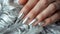 Glamour woman hand with luxury silver color nail polish manicure on fingers, touching silver feathers