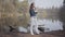 Glamour woman in white pants, jeans jacket and sunglasses standing on the riverbank. The girl is cold, she rubbing her