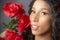 Glamourous studio portrait of young Latina woman holding red flowers