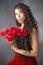 Glamourous studio portrait of young Latina woman holding red flowers