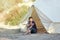 Glamping outdoor vacation. Woman drinking tea near big camping tent with cozy interior. Luxury travel accomodation into the forest