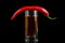 Glass with alcohol, top pod of bitter chili peppers, isolated on black