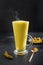 Glass of ayurvedic golden turmeric latte milk with curcuma powder on black . Vertical shot