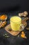 Glass of ayurvedic golden turmeric latte milk with curcuma root, powder on black. Vertical shot