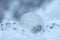 The glass ball lies on a dirty snowdrift or icy background with sunbeams. Weather and pollution concept.